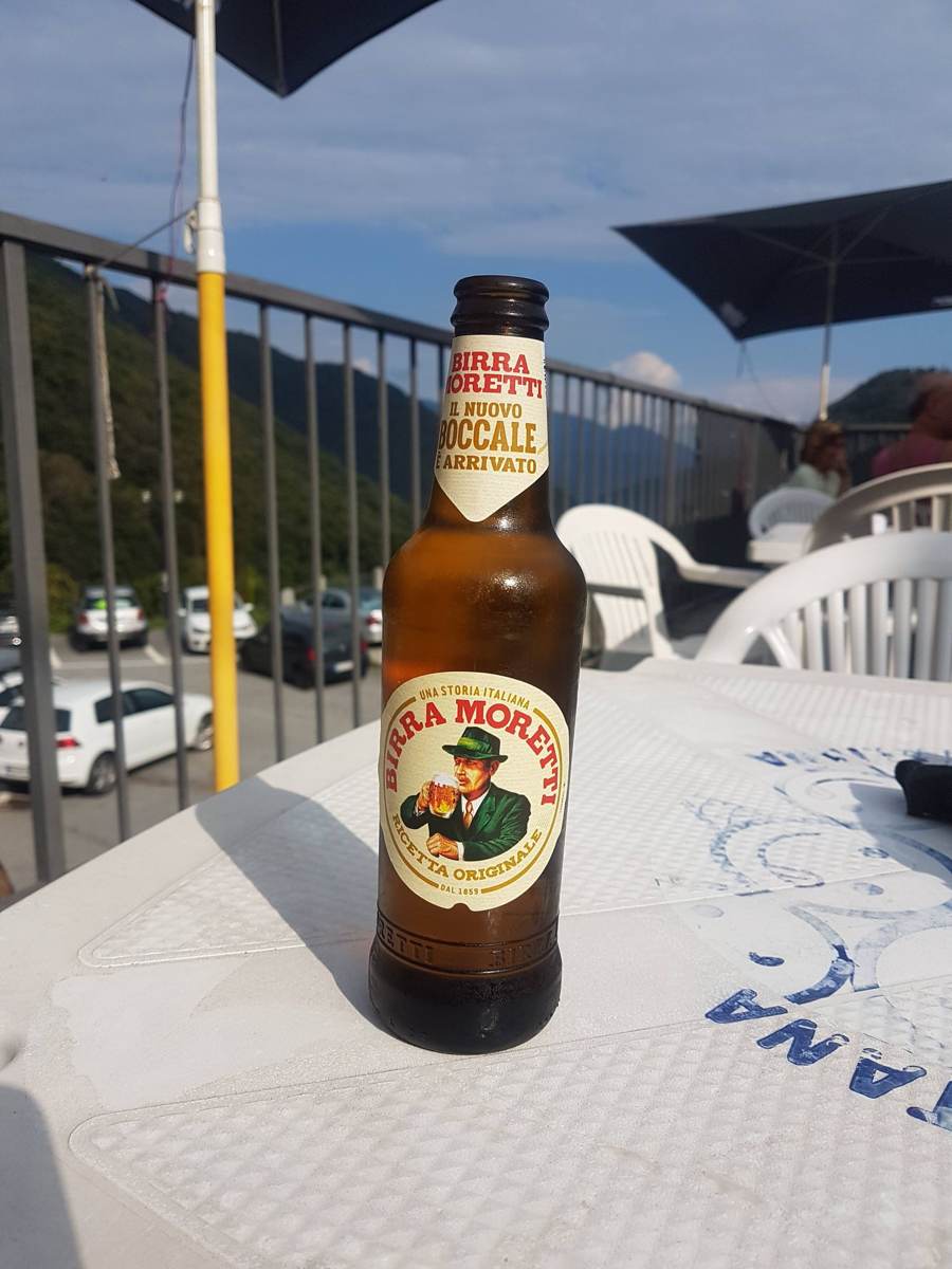 A bottle of Moretti beer on a table on a bar terrace overlooking the valley