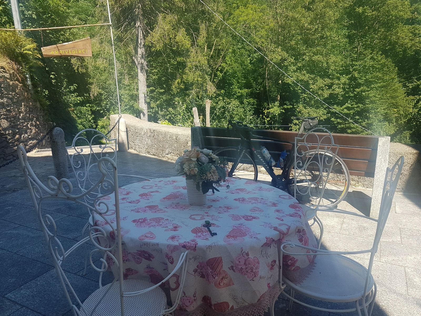A round café table with a pink rose-patterned tablecloth and white chairs on a terrace