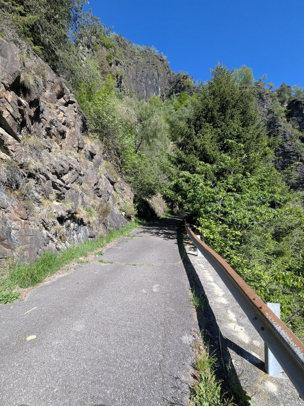 The narrow valley road running under overhanging rock with a crash barrier