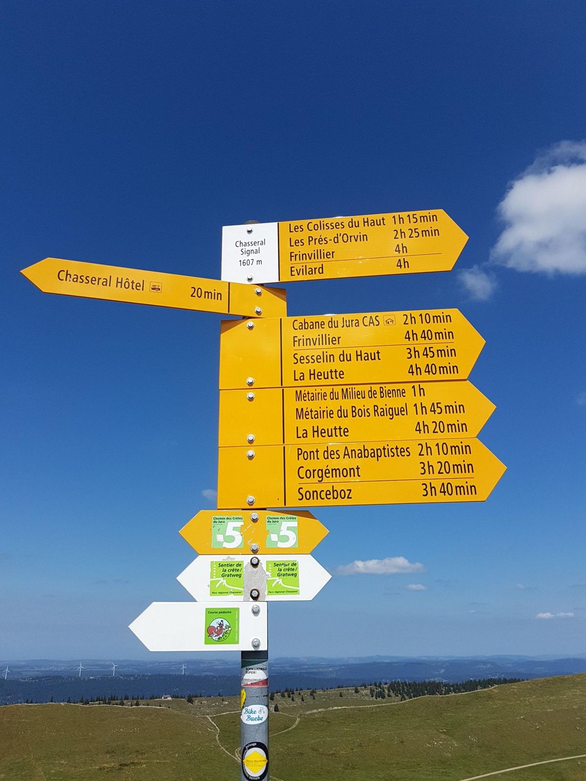 Yellow Swiss hiking signposts at the top of Chasseral pointing to Nods, Lignières, La Neuveville and other places