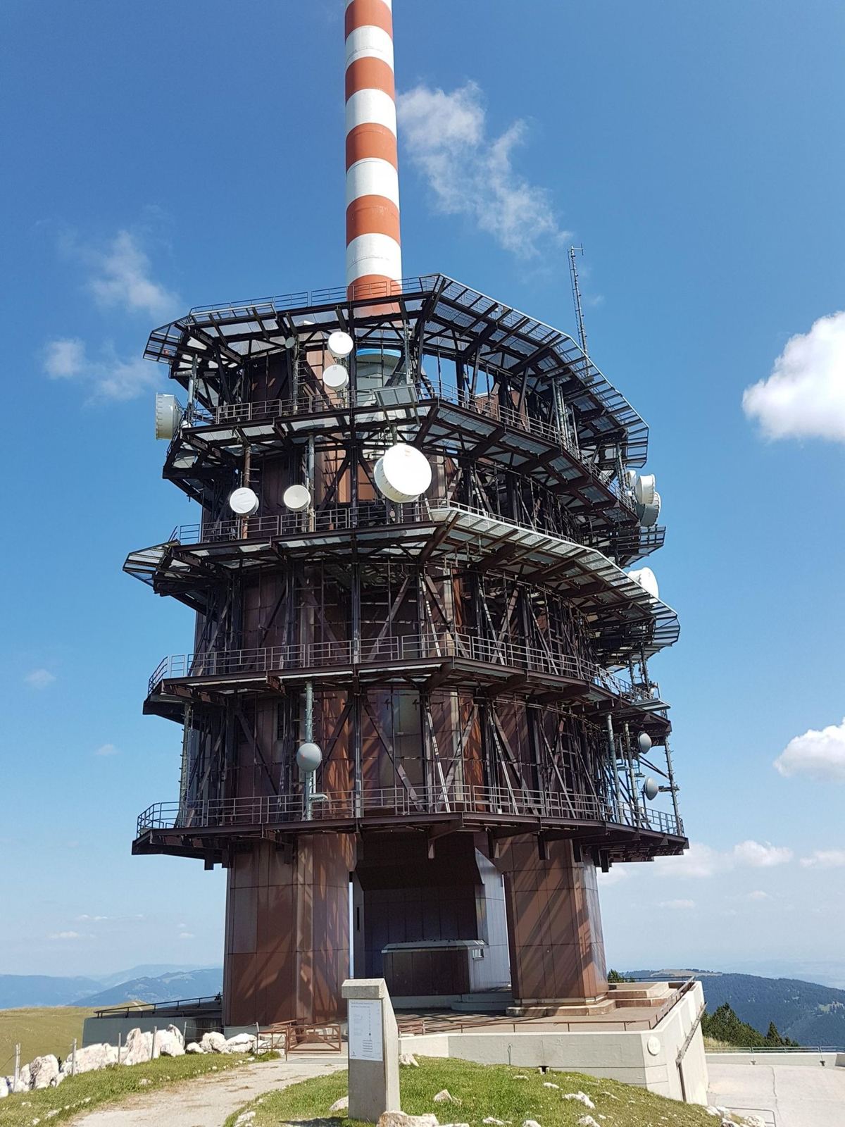 The red-and-white Swisscom transmitter tower at the top of Chasseral against a blue sky