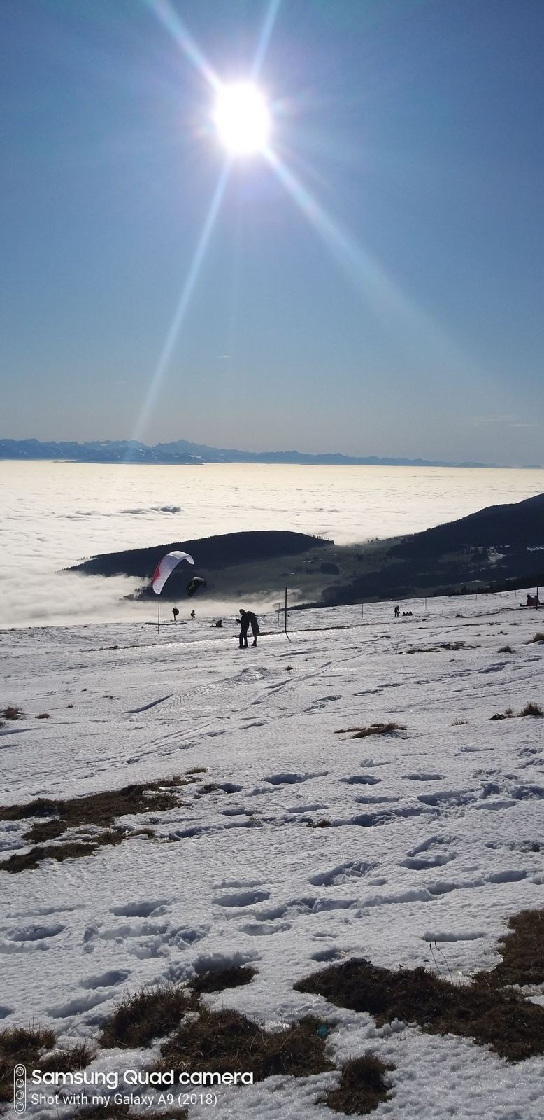 Deep snow at the top of Chasseral under a bright winter sun, with walkers and a sea of cloud below