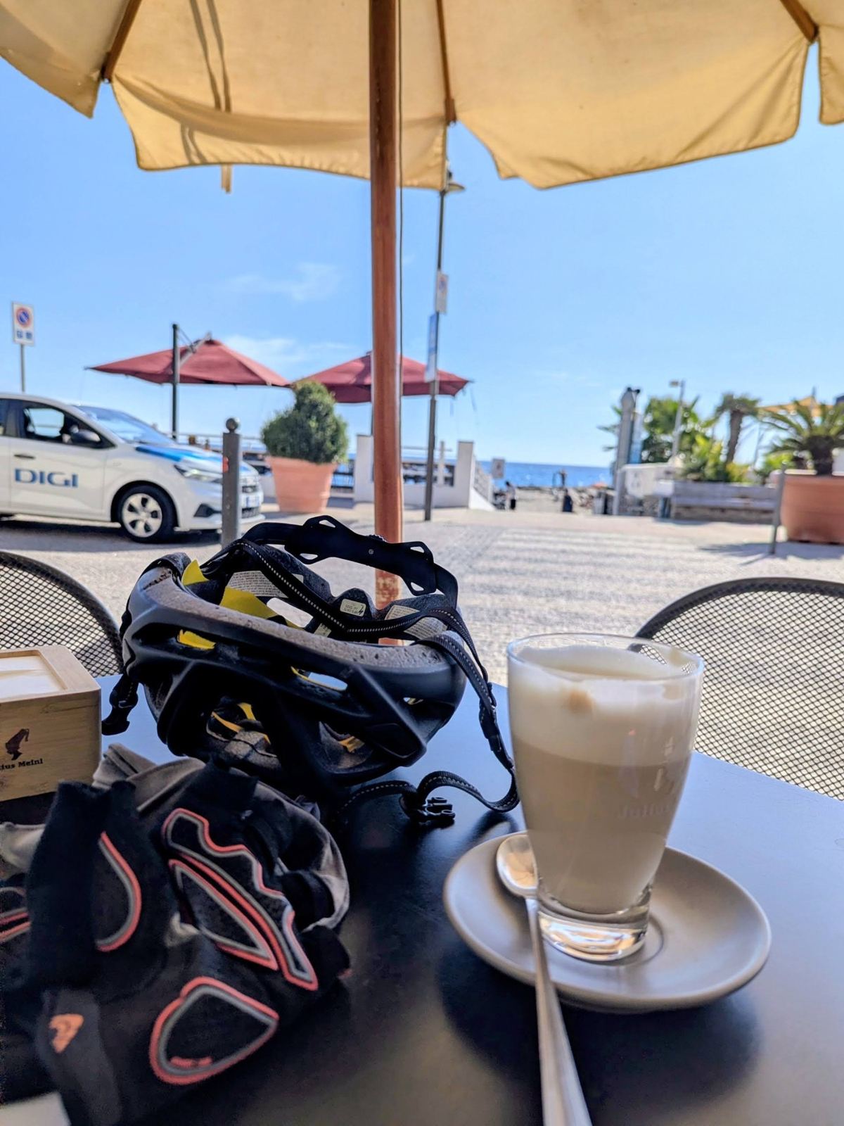 A latte and a cycling helmet on a café table by the sea at Santo Stefano al Mare