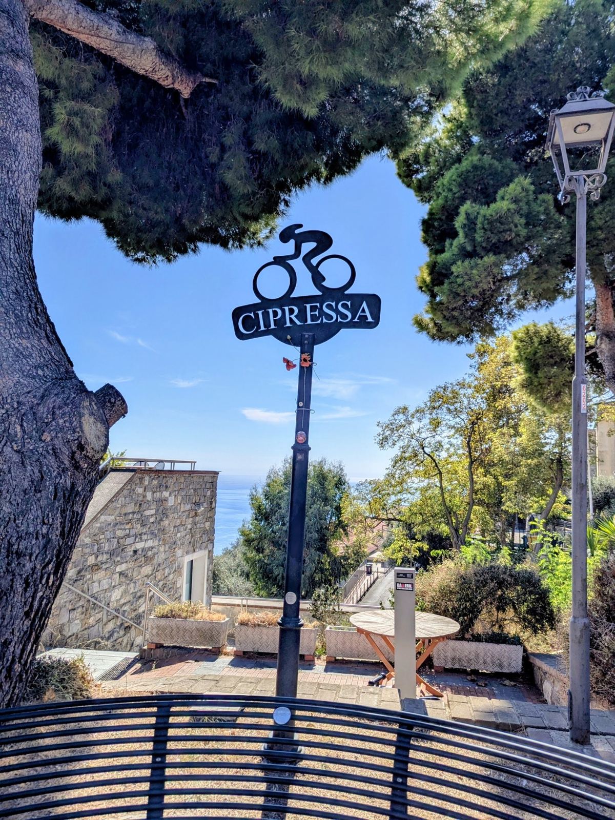 A cycling sign shaped like a rider with the name Cipressa, by the road at the top of the climb