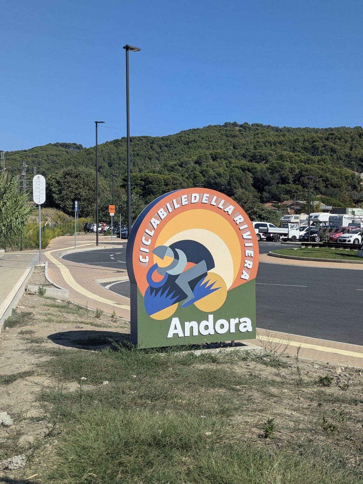 The cycle path sign for Andora beside the path, with the hills behind