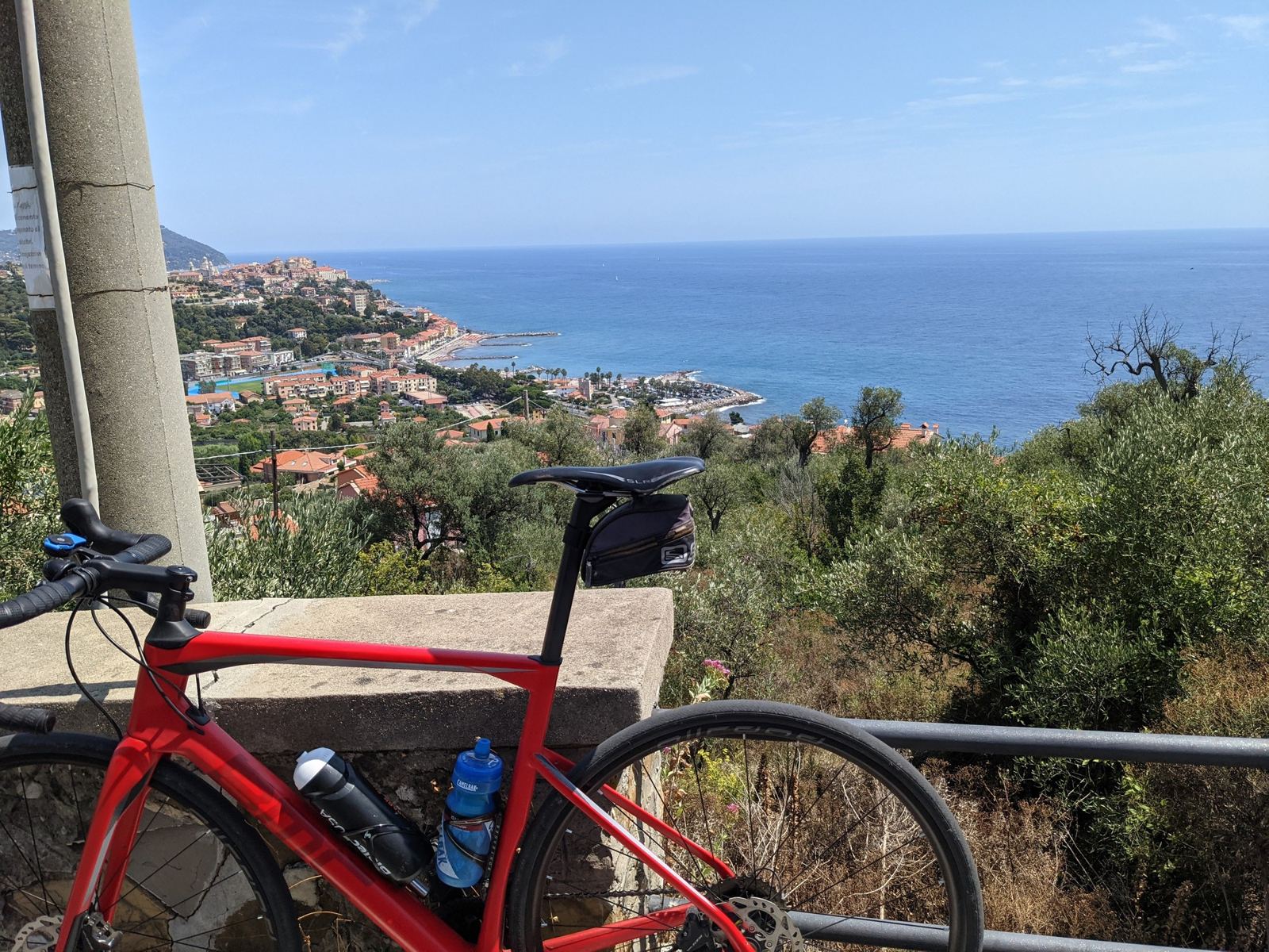 A red road bike against a railing with Porto Maurizio and the sea below