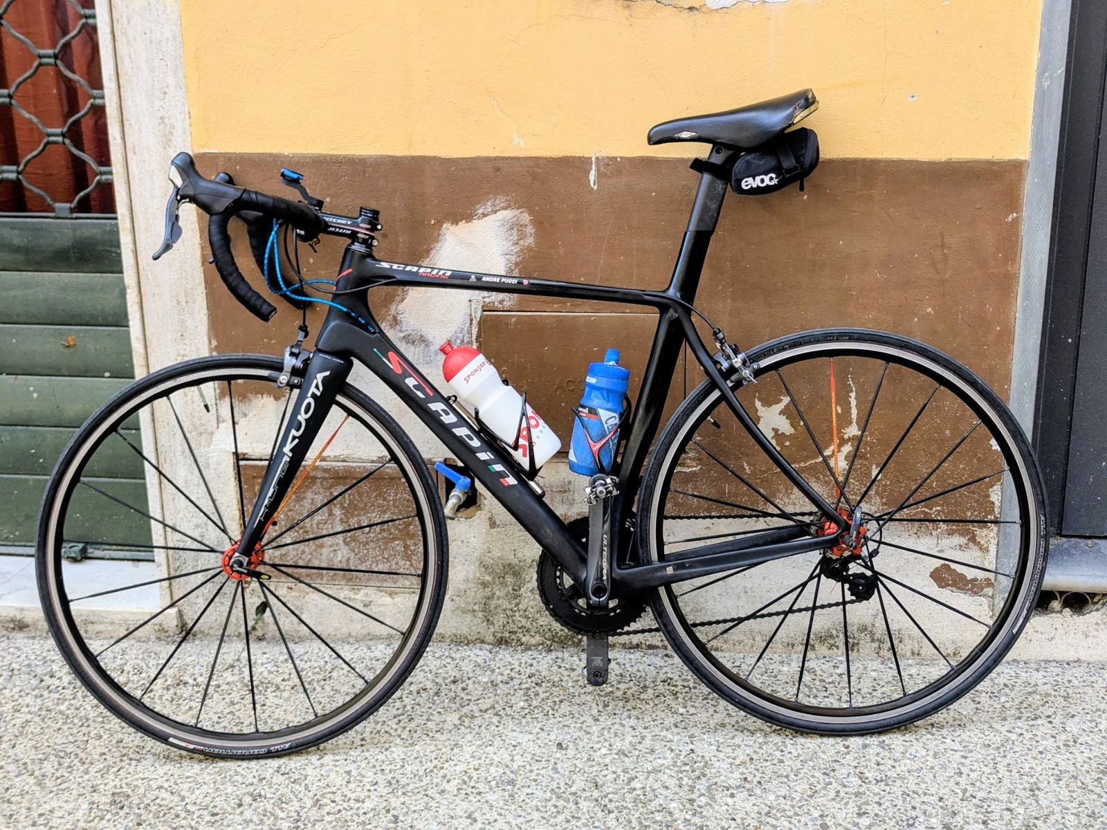 A black road bike leaning against a yellow wall in Dolcedo
