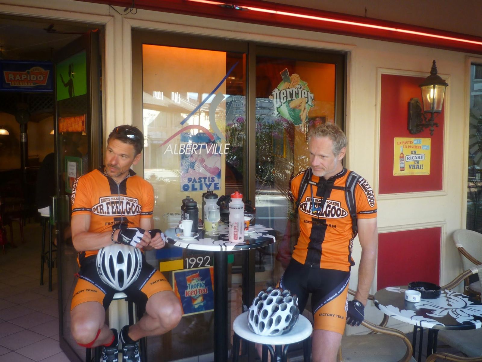 Two cyclists in orange Mr Feelgood jerseys at a café in Albertville