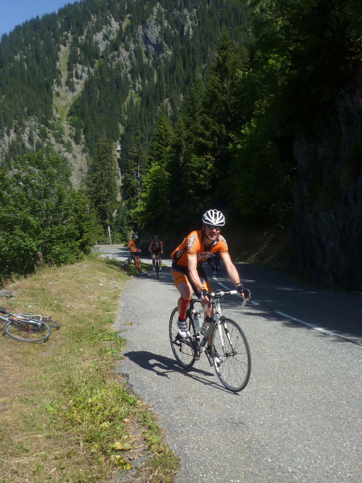 A cyclist in an orange jersey climbing towards the Cormet de Roselend through woods