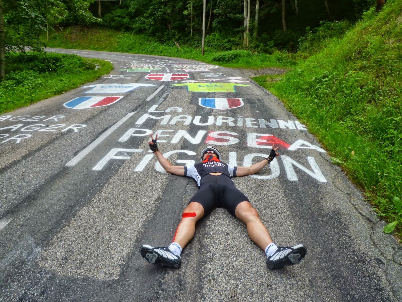 A cyclist lying on the road beside painted words La Maurienne pense à Fignon