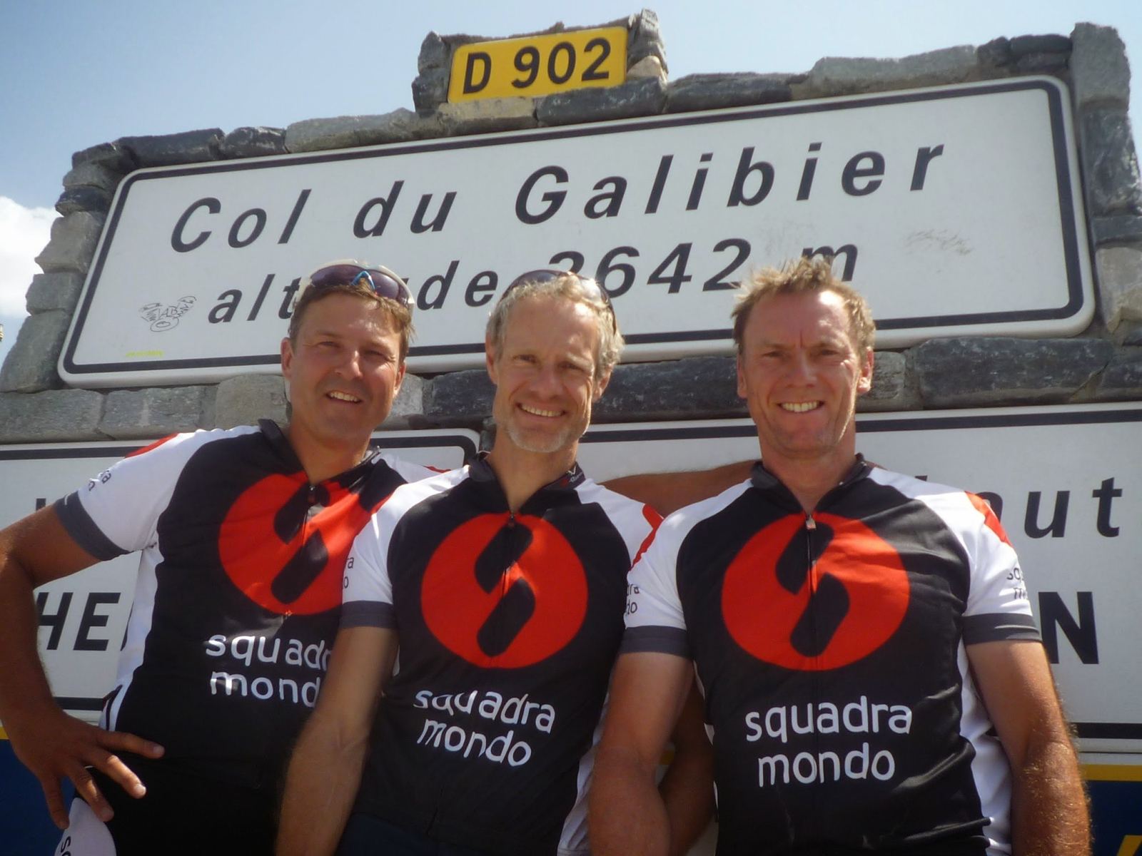 Three cyclists in Squadra Mondo jerseys at the Col du Galibier sign