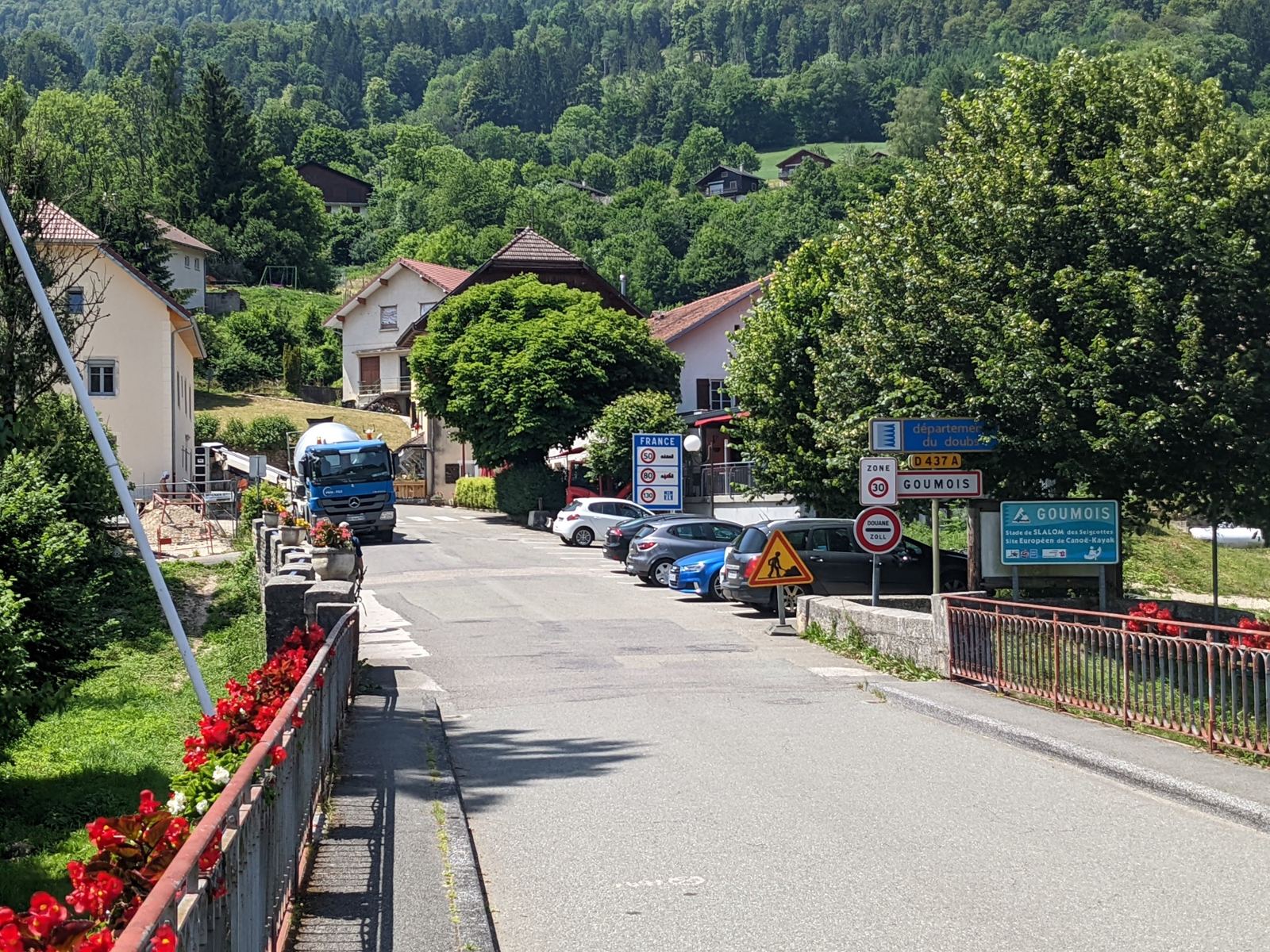 The main street of Goumois with flower boxes on the bridge railings and houses beyond