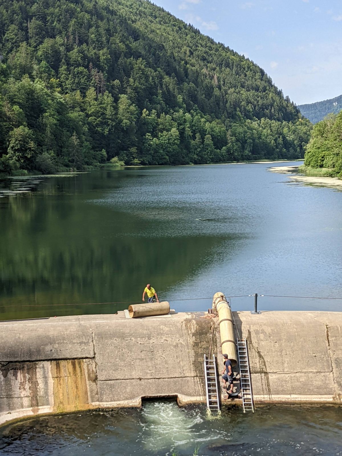 The concrete dam at La Goule with water spilling through, the green lake behind