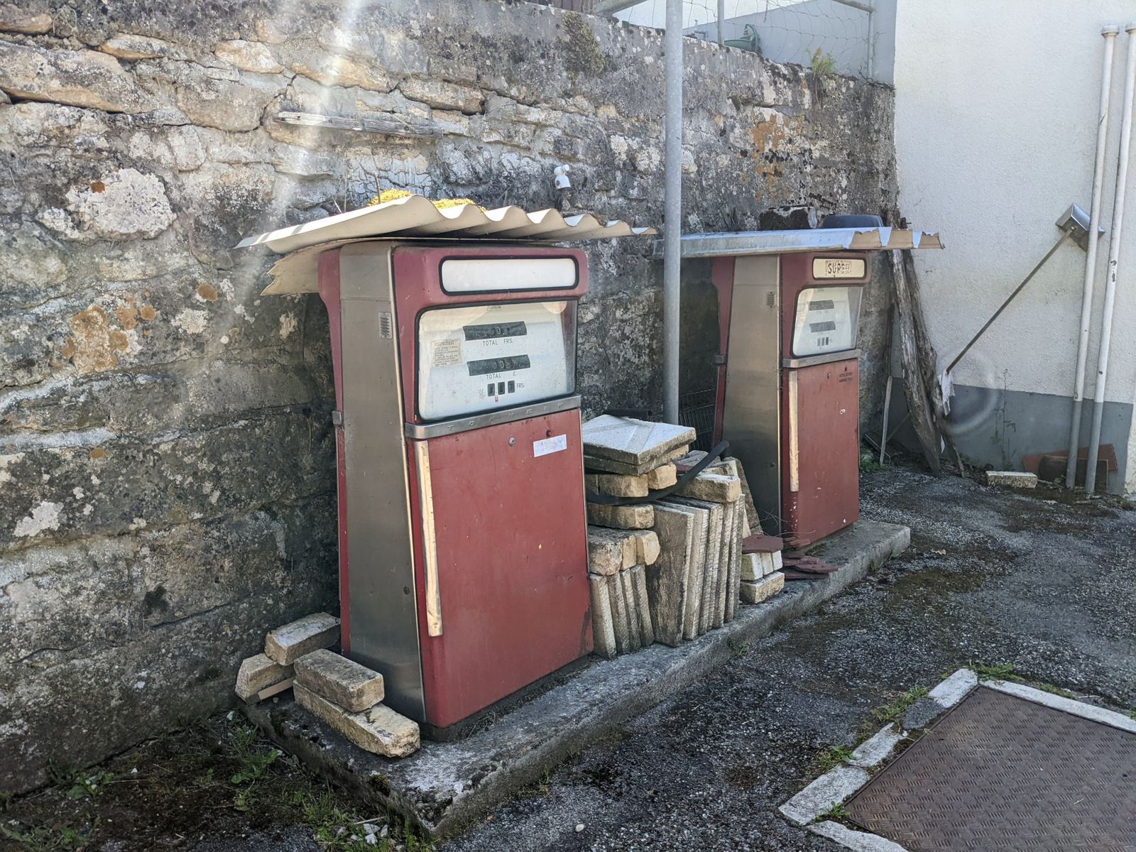 Two old red petrol pumps against a stone wall in Goumois