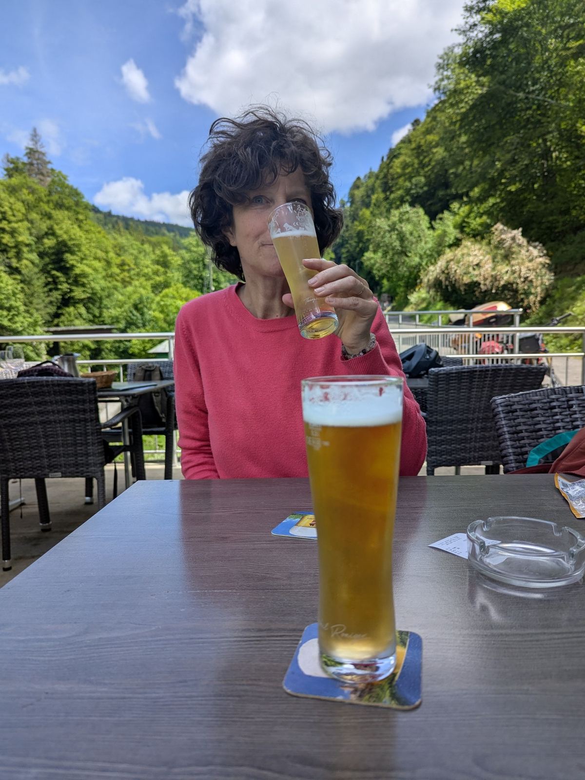 A woman holding a glass of beer on a terrace by the Doubs at La Goule