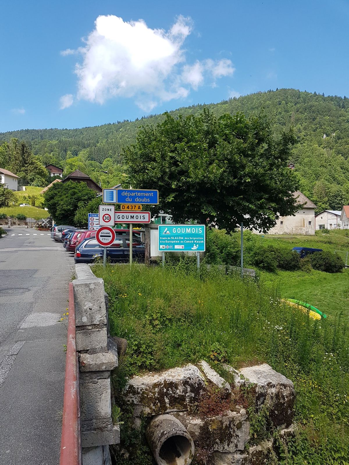 The road into Goumois by the border with road signs and the river bank