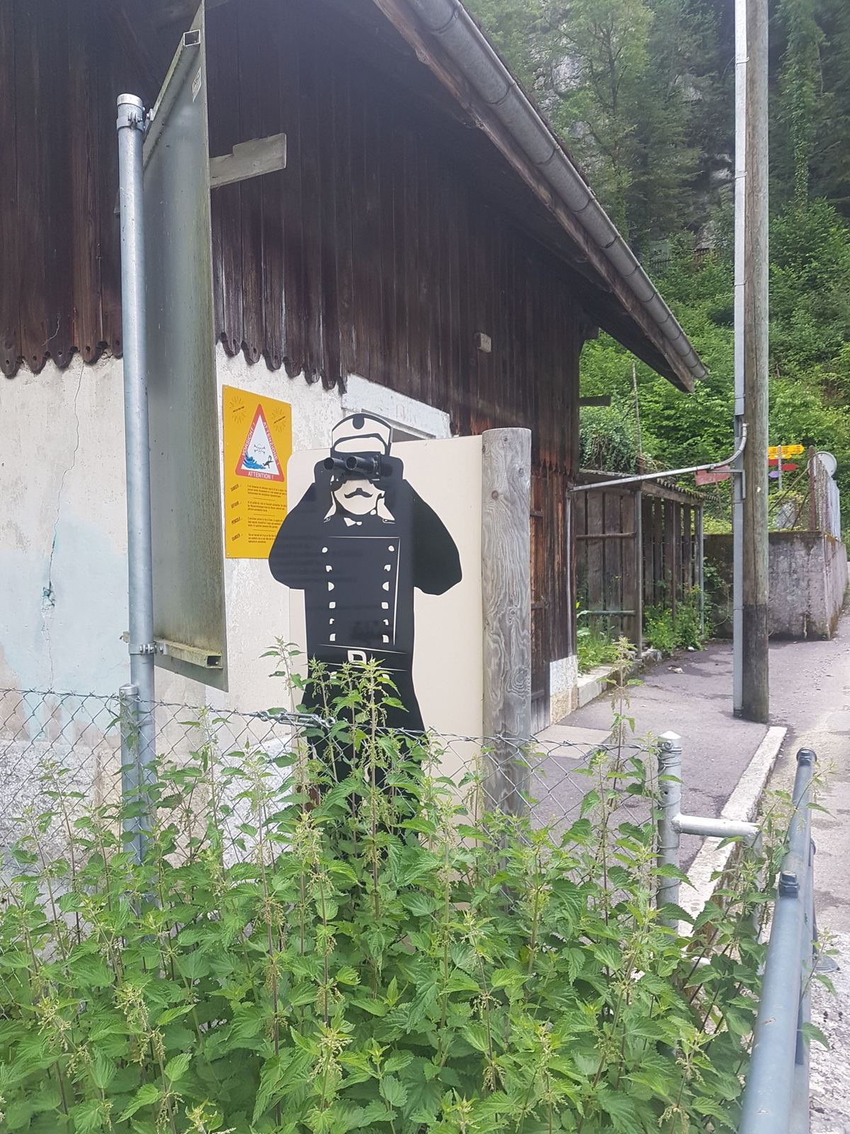 A carved wooden figure in a black cloak outside a building at La Goule