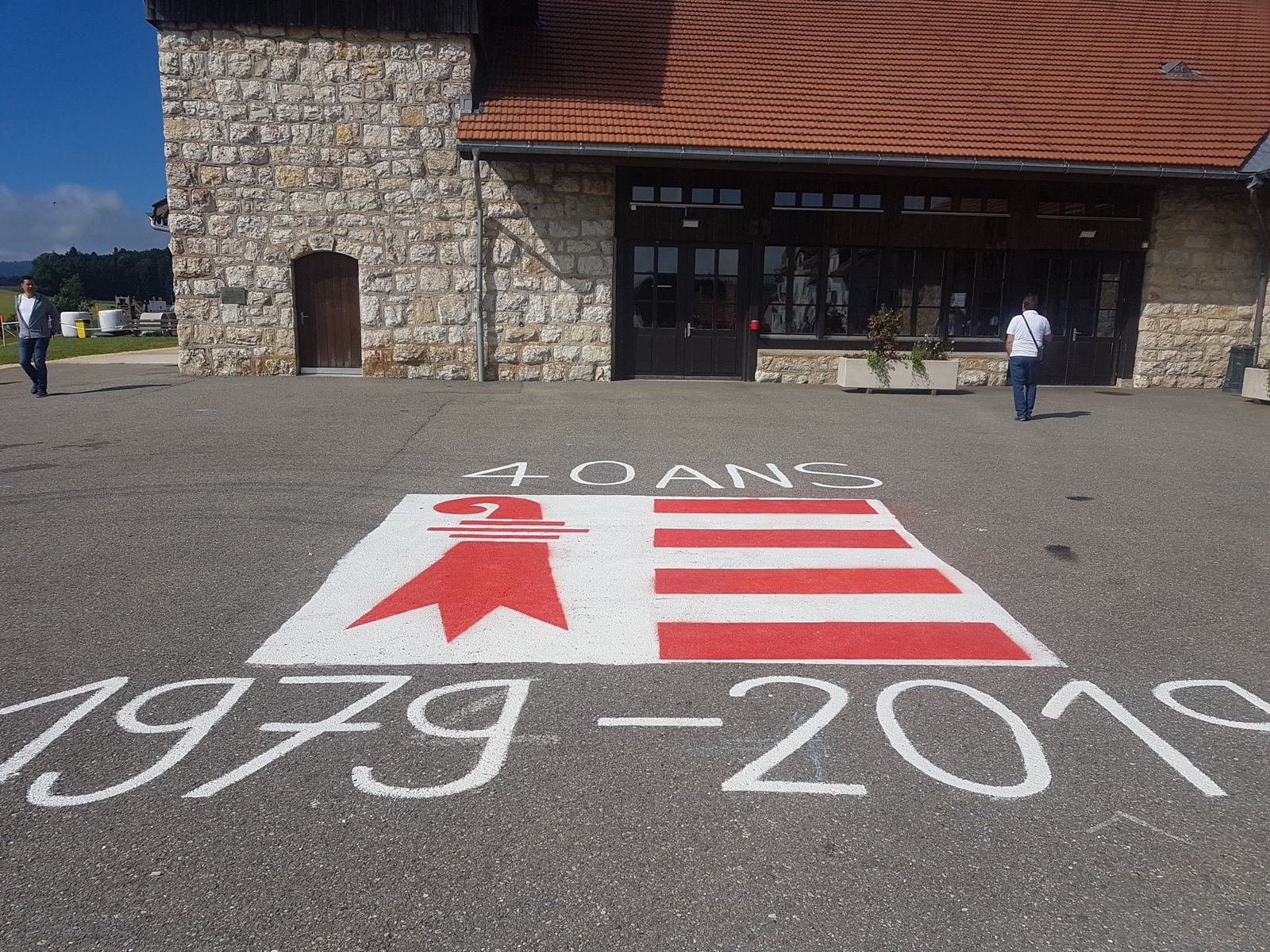 The stone Marché-Concours hall at Saignelégier with the Jura flag and '40 ans 1979-2019' painted on the square in front