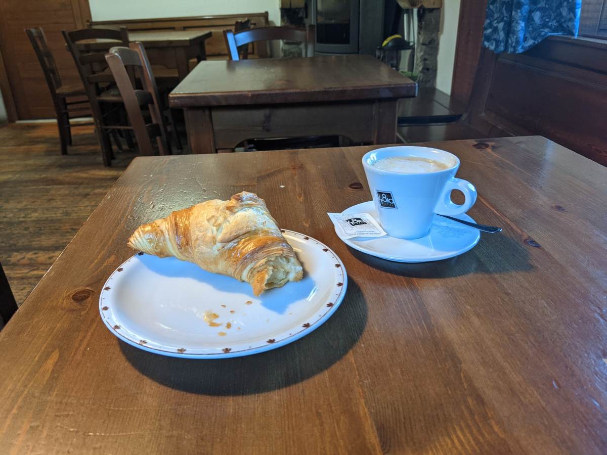 Coffee and a croissant on a wooden table inside a café at the Grand St Bernard Pass