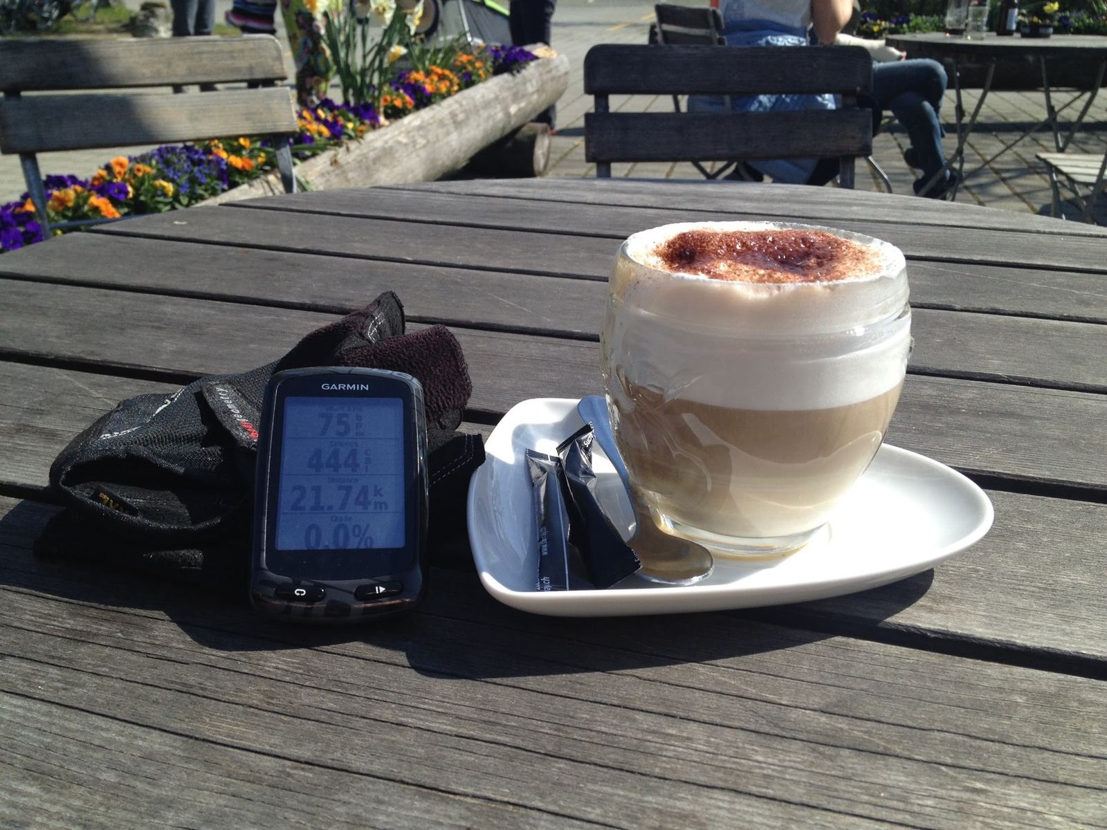 A cappuccino on a wooden table at the Erlach lakeside café next to a Garmin bike computer