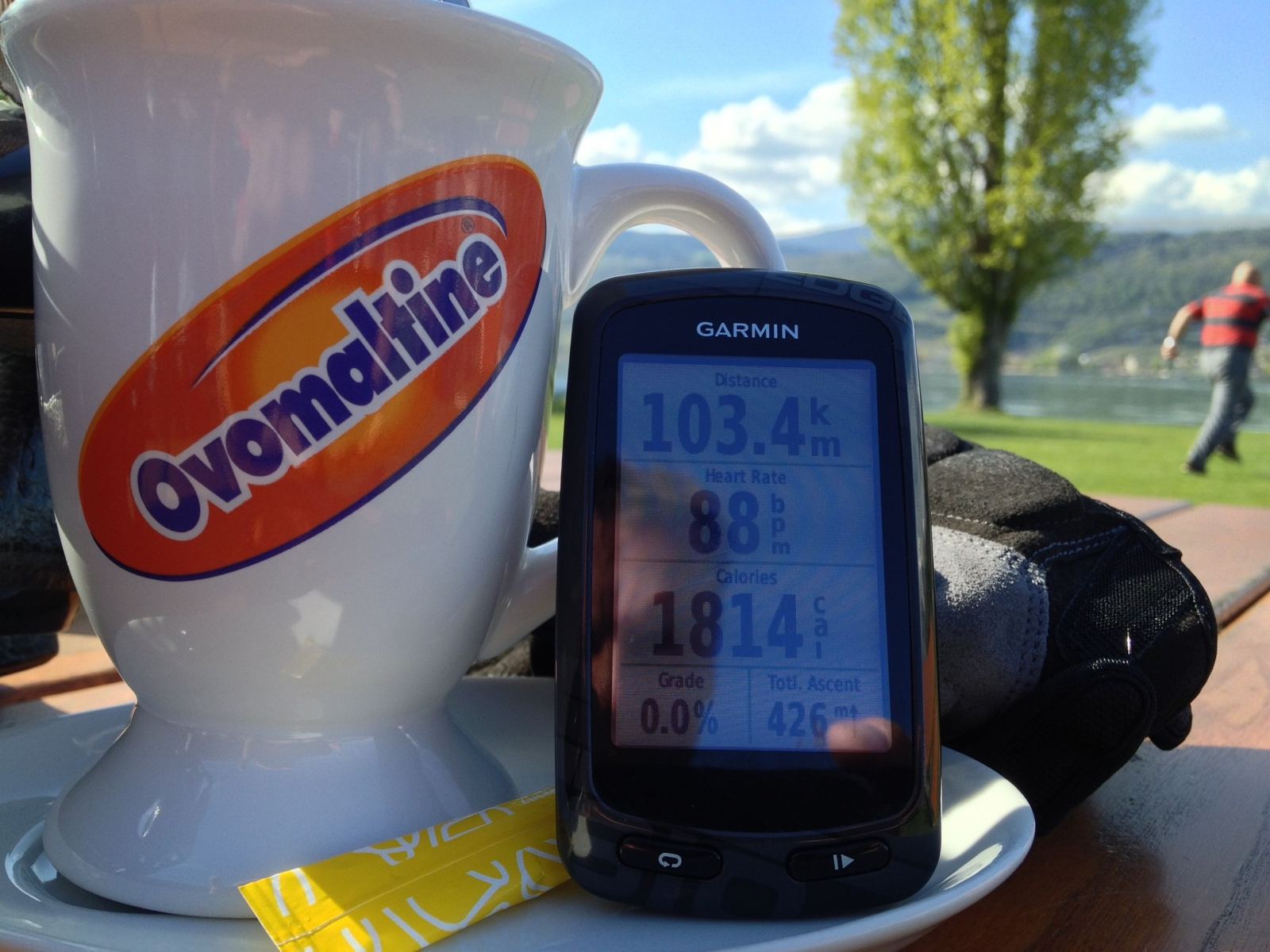 A large Ovomaltine mug next to a Garmin bike computer showing 103.4km, on a table at the Erlach lakeside café