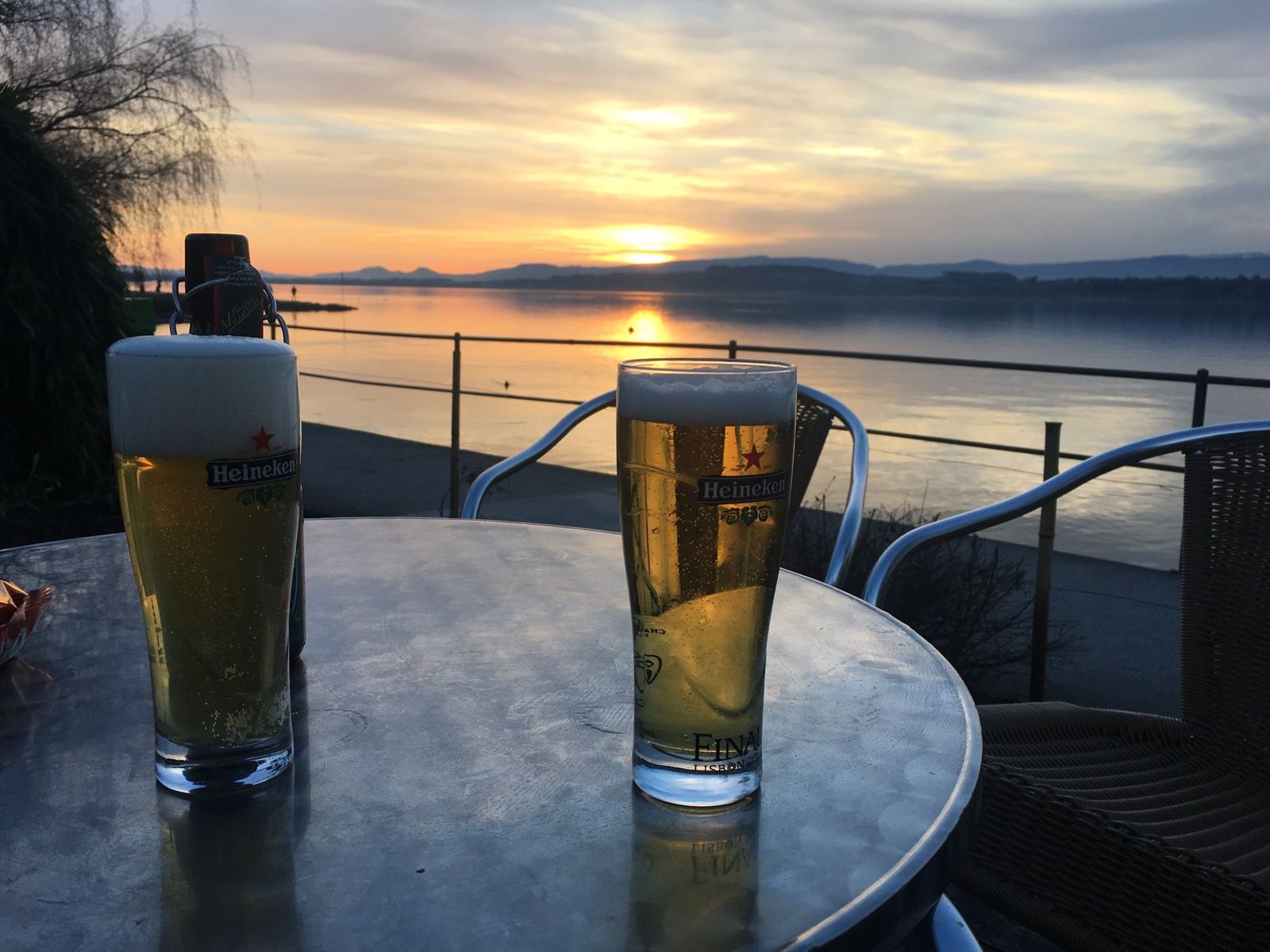 Two glasses of beer on a café table at Murten, with the sun setting over Lake Murten