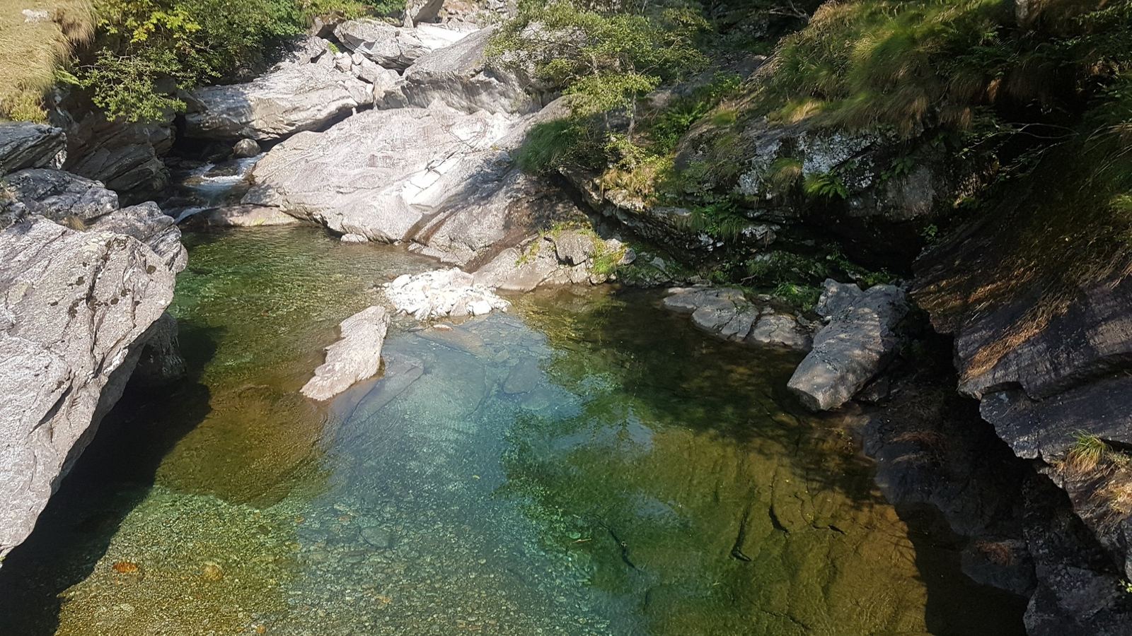 Clear green water in a deep pool between granite rocks, seen from above