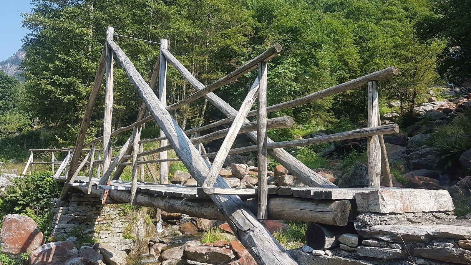 An old timber footbridge made of crossed logs over a rocky river