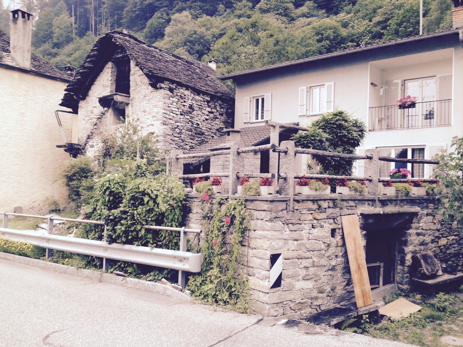 An old stone house and a newer house with flower boxes beside the valley road in the Verzasca