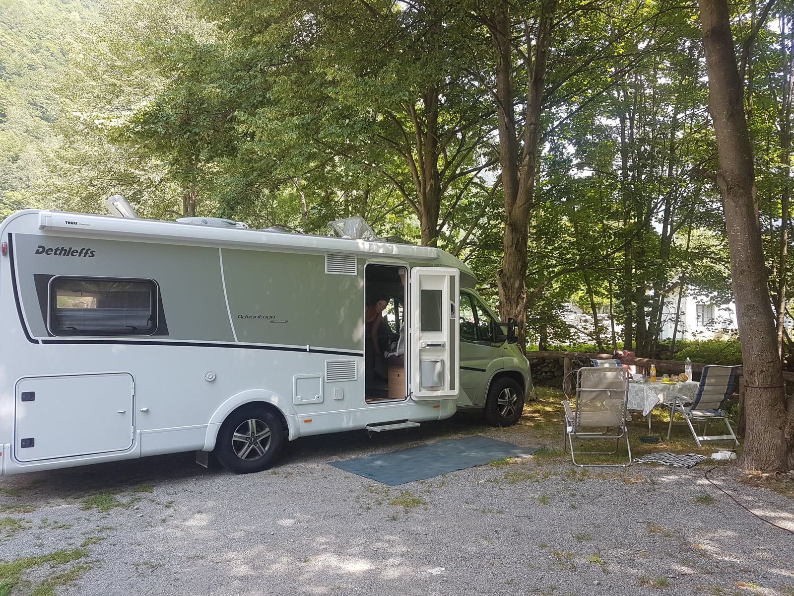 A motorhome parked under trees at a riverside campsite in the Verzasca valley