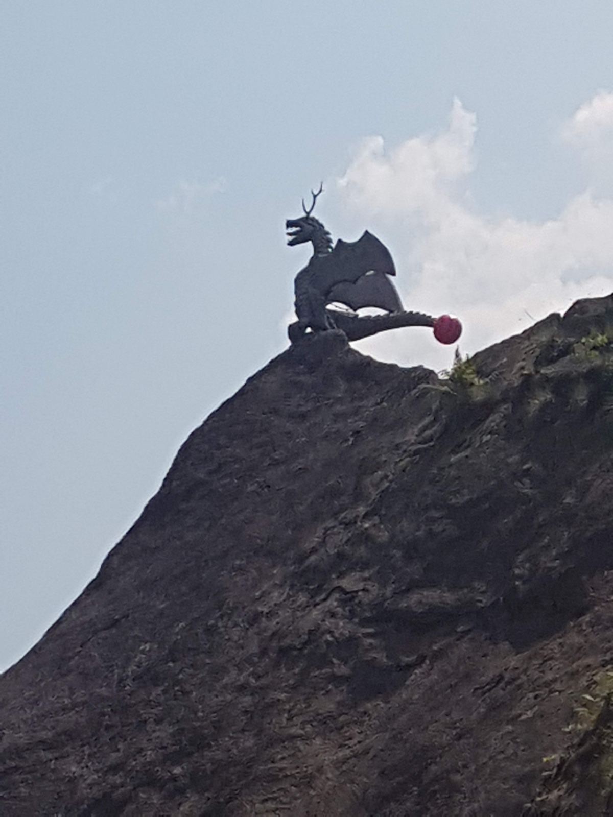 A dragon sculpture on top of a rock outcrop against the sky