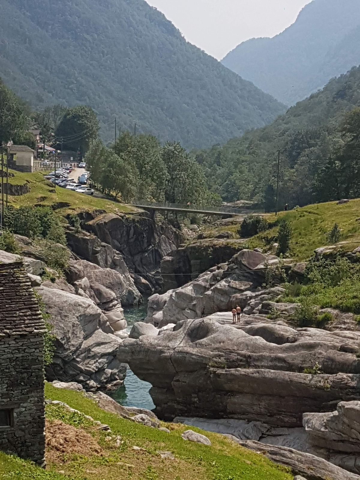 The Verzasca river running over white rocks with a stone bridge in the distance and green mountains